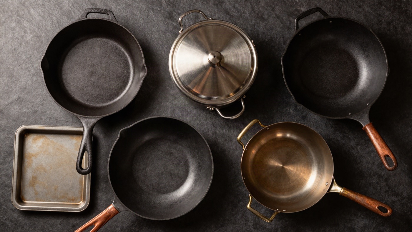 An overhead flat-lay of assorted cookware — a skillet, pot, wok, baking sheet, and saucepan